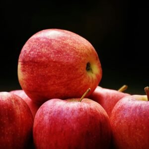 A cluster of ripe, red apples stacked on a dark backdrop highlighting their freshness and vibrancy.