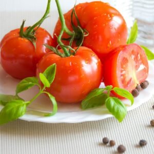 A fresh and vibrant display of tomatoes, basil, and peppercorns on a white plate, perfect for healthy cooking.